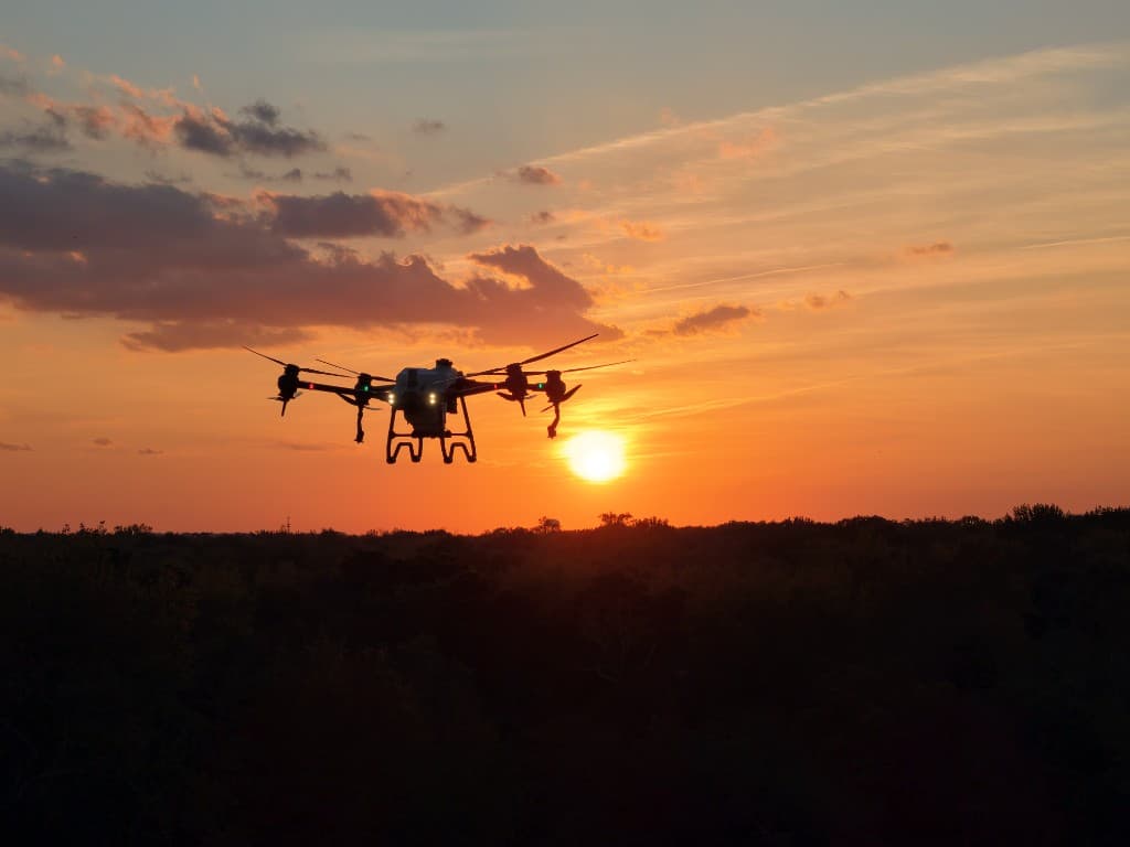 Agricultural drone silhouetted against a sunset sky